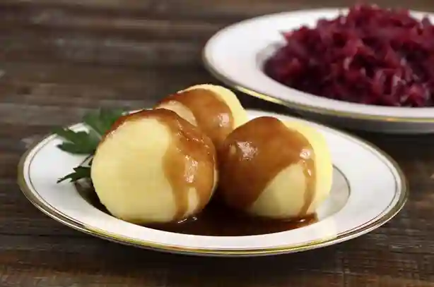 Drei Kartoffelklöße mit Sauce für Knödel auf einem Teller, serviert mit Rotkohl als Beilage.