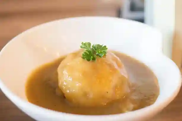 Ein Kartoffelkloß mit cremiger Sauce für Knödel, garniert mit frischer Petersilie, serviert in einer weißen Schale.