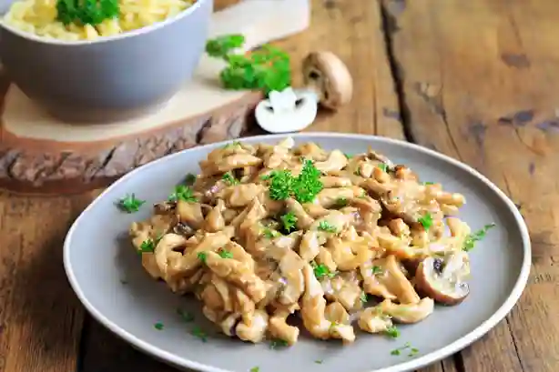 Spätzle mit Hähnchen in cremiger Soße mit Pilzen, serviert auf einem Teller, garniert mit frischer Petersilie.