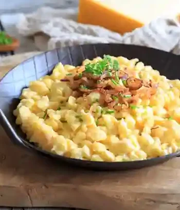 Schwäbische Käsespätzle Pfanne mit goldbraunen Röstzwiebeln, serviert in einer schwarzen Pfanne auf einem Holzbrett.