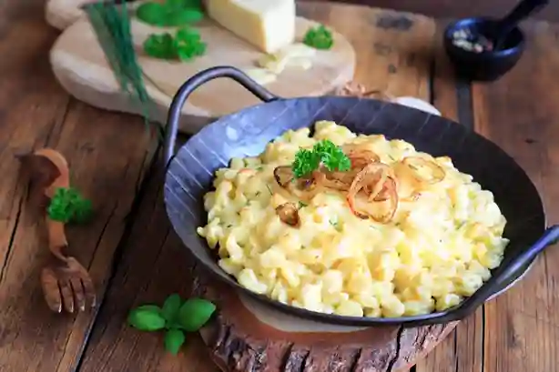 Schwäbische Käsespätzle Pfanne mit geschmolzenem Käse und knusprigen Röstzwiebeln, serviert in einer schwarzen Pfanne auf einem rustikalen Holztisch.