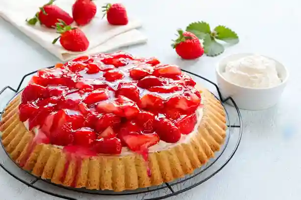 Ein klassischer Erdbeerkuchen mit Biskuitboden, garniert mit frischen Erdbeeren und einer glänzenden Fruchtschicht, serviert mit Schlagsahne.