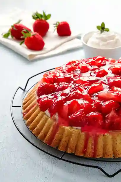 Ein köstlicher Erdbeerkuchen mit Biskuitboden, belegt mit frischen Erdbeeren und glänzendem Fruchtspiegel, serviert mit Schlagsahne.