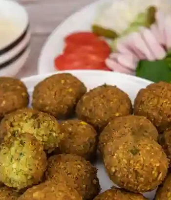 Frisch gebratene Falafel nach traditionellem Falafel Rezept mit Beilagen wie Tomaten, Zwiebeln, Kräutern und Joghurtsauce auf einem Teller serviert.