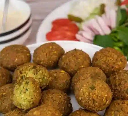 Frisch gebratene Falafel nach traditionellem Falafel Rezept mit Beilagen wie Tomaten, Zwiebeln, Kräutern und Joghurtsauce auf einem Teller serviert.