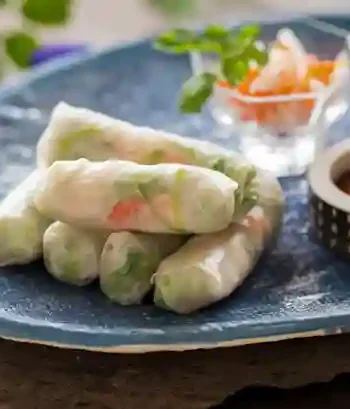 Sommerrollen Rezept mit Garnelen und frischem Gemüse, serviert auf einem blauen Teller mit Dipsauce und Kräutern