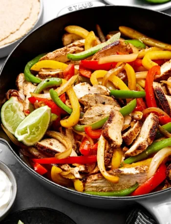 Hähnchen Fajita​s mit buntem Gemüse und Limette in einer Pfanne.