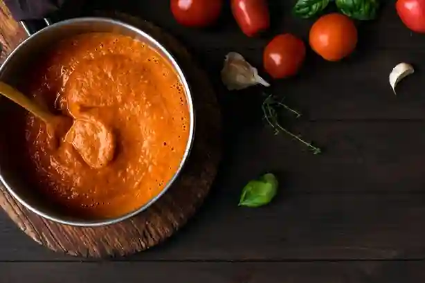 Tomaten Sahne Soße in einem Topf, umgeben von frischen Tomaten, Knoblauch und Basilikum.