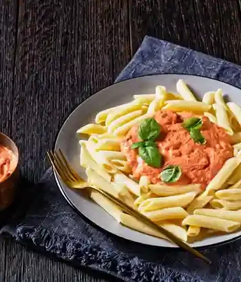 Pasta mit cremiger Tomaten Sahne Soße und frischem Basilikum auf einem Teller angerichtet.
