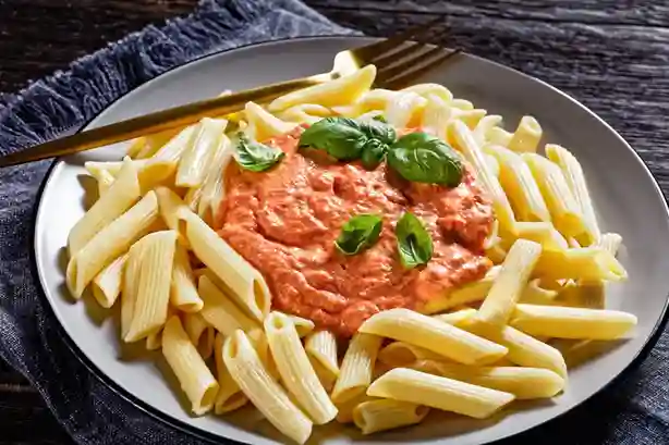 Penne mit cremiger Tomaten Sahne Soße und Basilikum auf einem Teller serviert.
