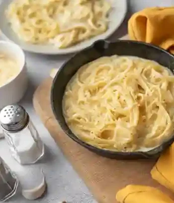 Pasta mit Parmesan Sahne Soße in einer Pfanne serviert, garniert mit frisch geriebenem Parmesan.