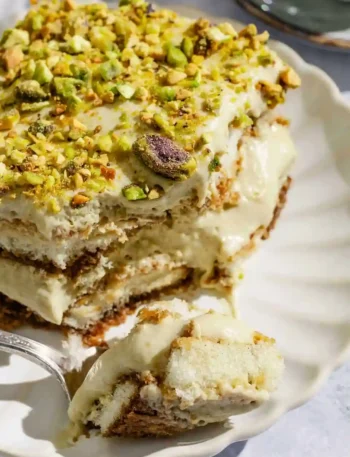 Nahaufnahme von cremigem pistazien tiramisu mit gehackten Pistazien auf einem weißen Teller.