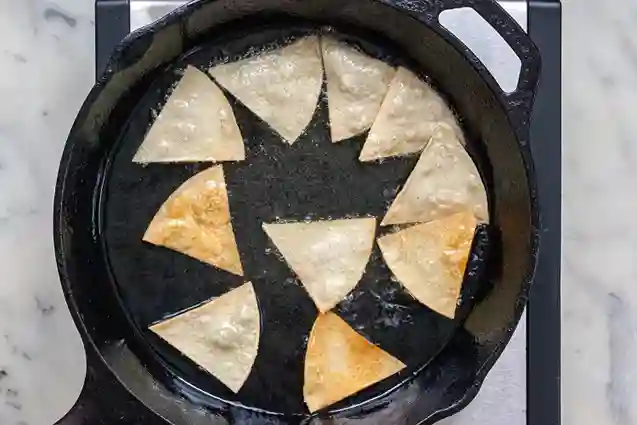 Tortilla Chips selber machen: Tortilla triangles frying in a cast-iron skillet.