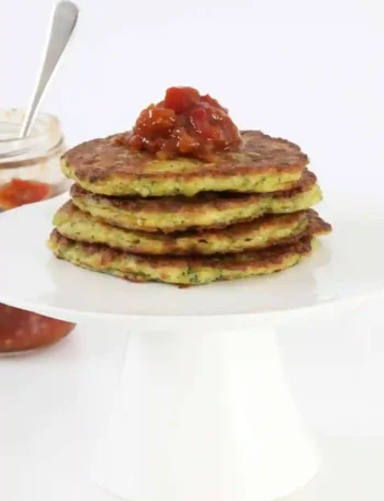Frisch gebratene zucchinipuffer thermomix gestapelt auf einem Teller mit Chutney-Topping.