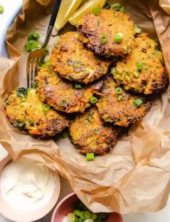 Knusprige zucchini möhren puffer mit Frühlingszwiebeln und Zitronenspalten serviert.