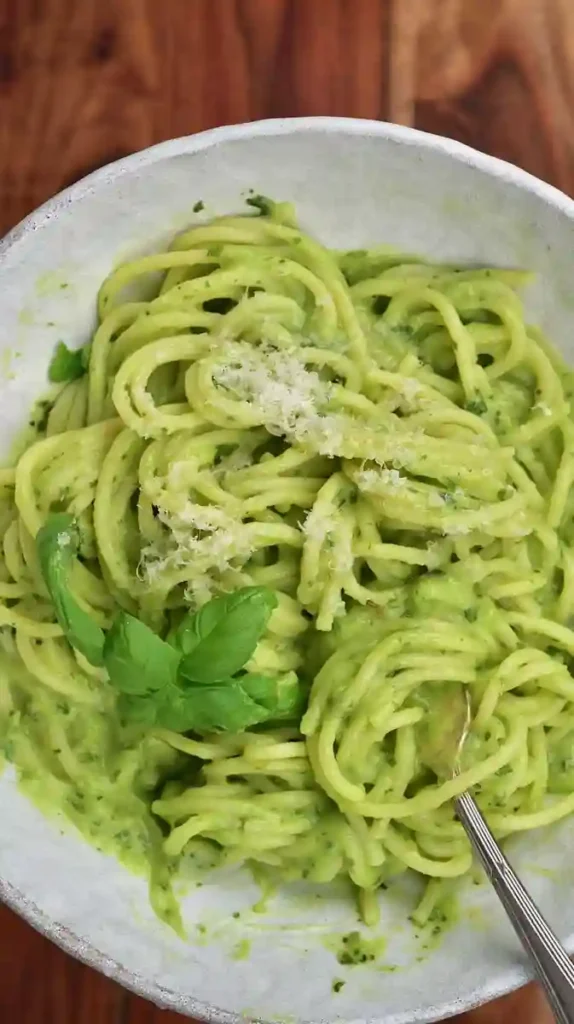 A close-up view of spaghetti avocado pasta, topped with grated parmesan and fresh basil.