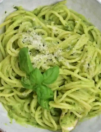Cremige Avocado Pasta mit Parmesan und frischen Basilikumblättern in einer Schüssel.