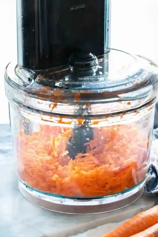 Karotten werden mit der Küchenmaschine geraspelt für Omas Möhrensalat mit Apfel und Zitrone