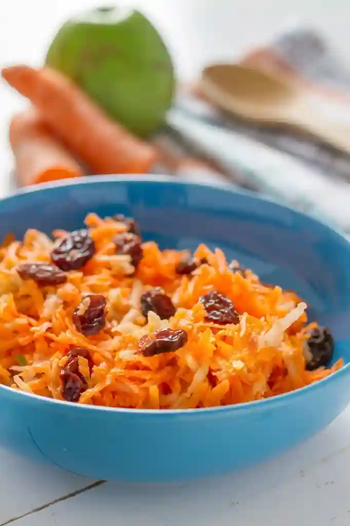 Omas Möhrensalat mit Apfel und Zitrone mit Rosinen in blauer Schüssel serviert