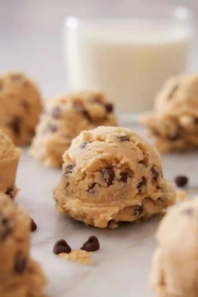 Essbarer cookie dough rezept – Kugeln roher Keksteig mit Schokodrops auf Marmorplatte, perfekt zum Löffeln.