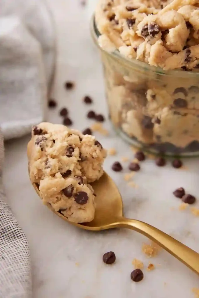 Essbarer Keksteig auf goldener Löffel – cookie dough rezept mit Schokodrops im Glas angerichtet.