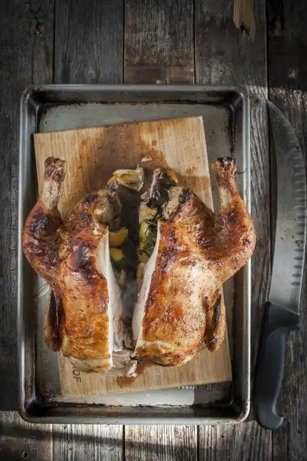 Frisch gegartes halbes Hähnchen im Backofen, auf einem Holzbrett halbiert und gefüllt mit Zitrone, Kräutern und Knoblauch – perfekt für ein traditionelles Hähnchenrezept aus dem Ofen.