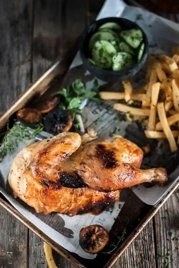 Halbes Hähnchen mit Pommes und Gurkensalat auf Backblech serviert – knusprig gebraten im Backofen.