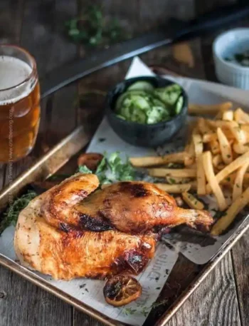 Halbes Hähnchen im Backofen mit knuspriger Haut, serviert mit Pommes und Gurkensalat auf einem Blech – traditionell wie vom Biergarten oder Oktoberfest.