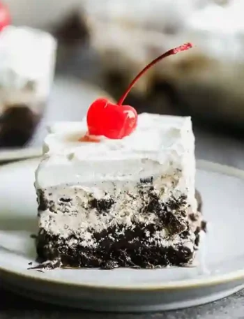Eistorte selber machen mit Schokoboden, Eiscreme-Schicht und Sahne – dekoriert mit einer Cocktailkirsche auf einem Dessertteller