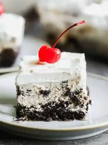 Eistorte selber machen mit Schokoboden, Eiscreme-Schicht und Sahne – dekoriert mit einer Cocktailkirsche auf einem Dessertteller