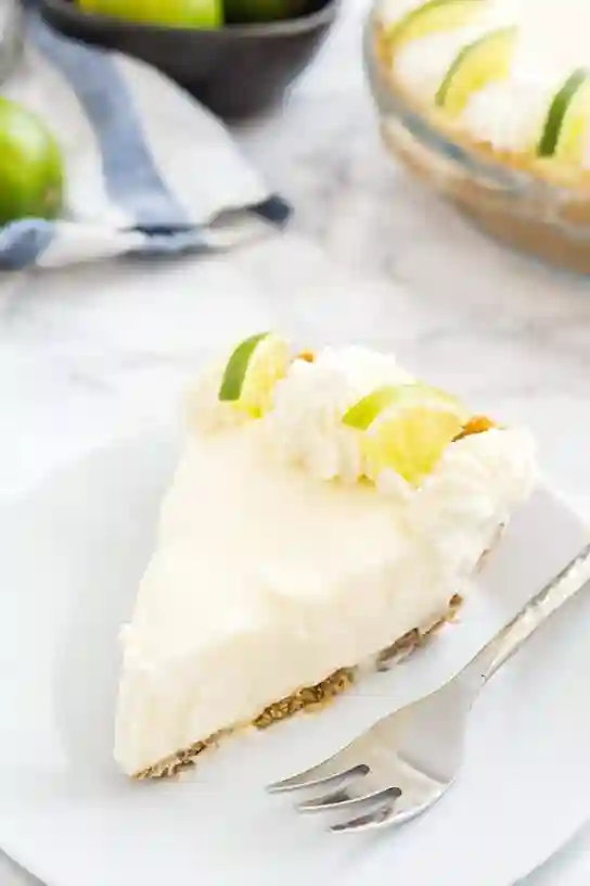 Stück vom No Bake Key Lime Pie Rezept mit Limetten und Sahne auf einem weißen Teller
