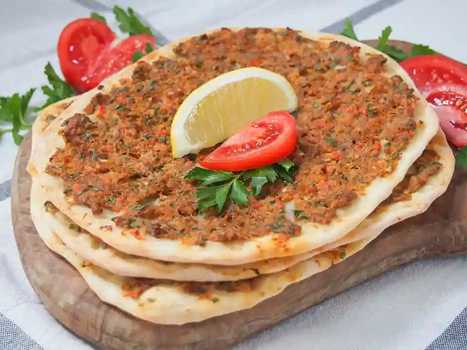 Lahmacun selber machen – türkische Pizza mit Hackfleisch, Tomaten, Petersilie und Zitrone auf Holzbrett serviert.