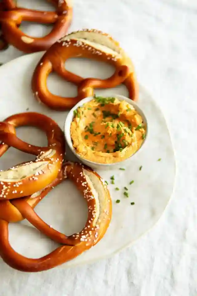 Bayerischer Obatzter mit frischer Laugenbrezel auf weißem Teller serviert
