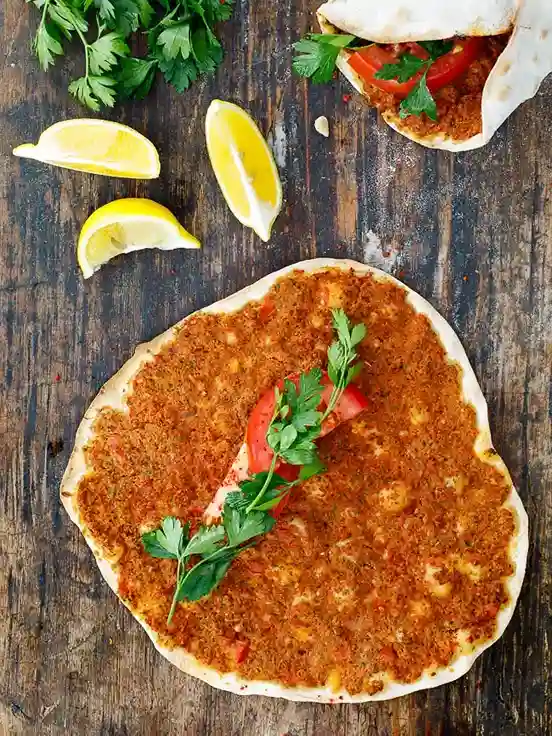 Lahmacun Turkish Pizza mit Hackfleischfüllung, Petersilie und Tomate – türkische Pizza zum selber machen mit Zitrone serviert.