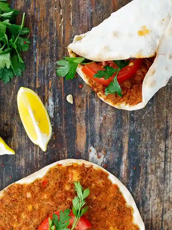 Gerollter Lahmacun mit Hackfleischfüllung, frischer Petersilie und Tomate – türkische Pizza selber machen mit Zitrone serviert.