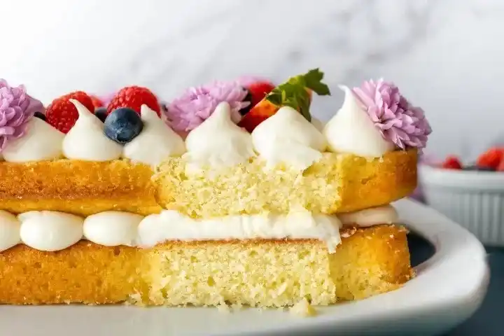 Anschnitt einer Zahlentorte mit Biskuitboden und Vanillecreme, dekoriert mit Beeren und essbaren Blüten – luftiger Number Cake im Querschnitt