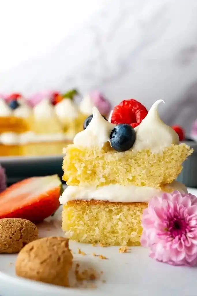 Anschnittstück einer Zahlentorte mit Biskuitboden, Frischkäsecreme, Beeren und essbarer Blüte – saftiger Number Cake im Detail