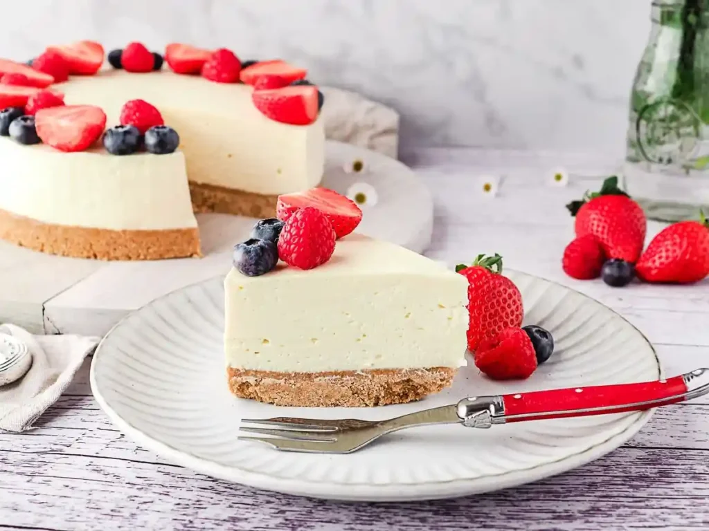 Philadelphia Kuchen ohne Backen mit Keksboden und Beeren, serviert auf einem Teller, im Vordergrund ein Stück mit Erdbeeren