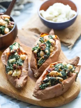 Gefüllte Süßkartoffeln mit Feta, Spinat und Bohnen im Ofen serviert auf Holzbrett