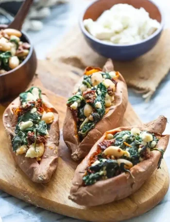 Gefüllte Süßkartoffeln mit Feta, Spinat und Bohnen im Ofen serviert auf Holzbrett