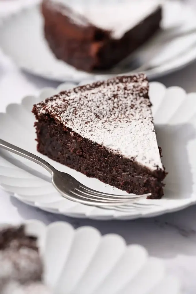 Ein Stück glutenfreier Schokoladenkuchen mit Puderzucker auf weißem Teller und Gabel