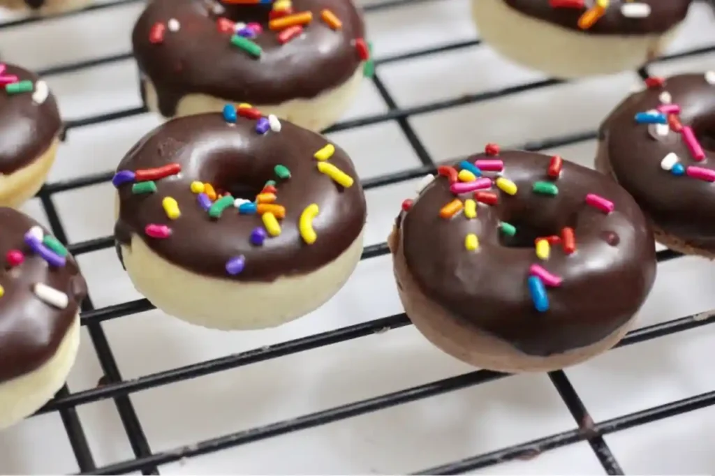 Mini Donuts mit Schokoglasur und bunten Streuseln auf einem Gitterrost frisch aus dem Backofen