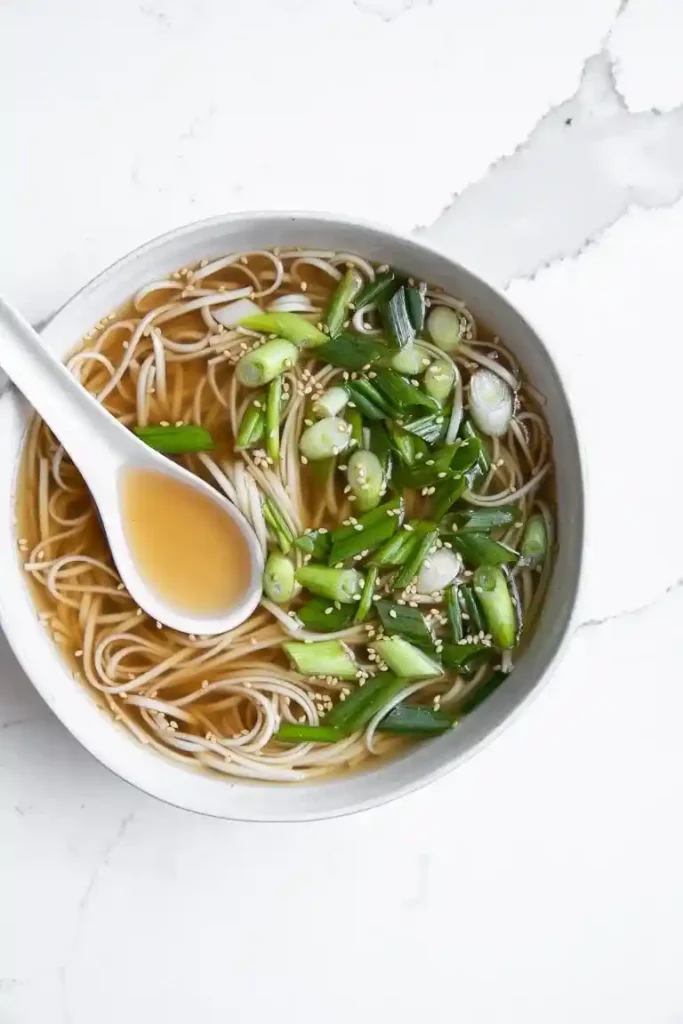 Nudelsuppe mit Frühlingszwiebeln und Knochensuppe aus Rinderknochen in einer weißen Schale