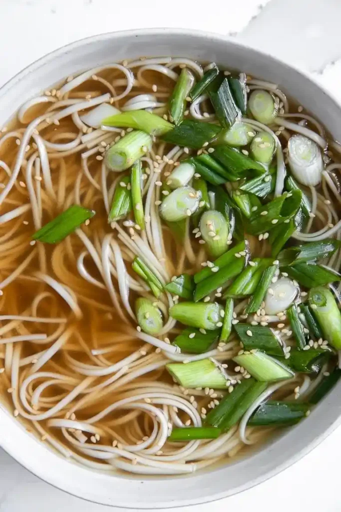 Schale mit Knochensuppe, Soba-Nudeln, Frühlingszwiebeln und Sesam