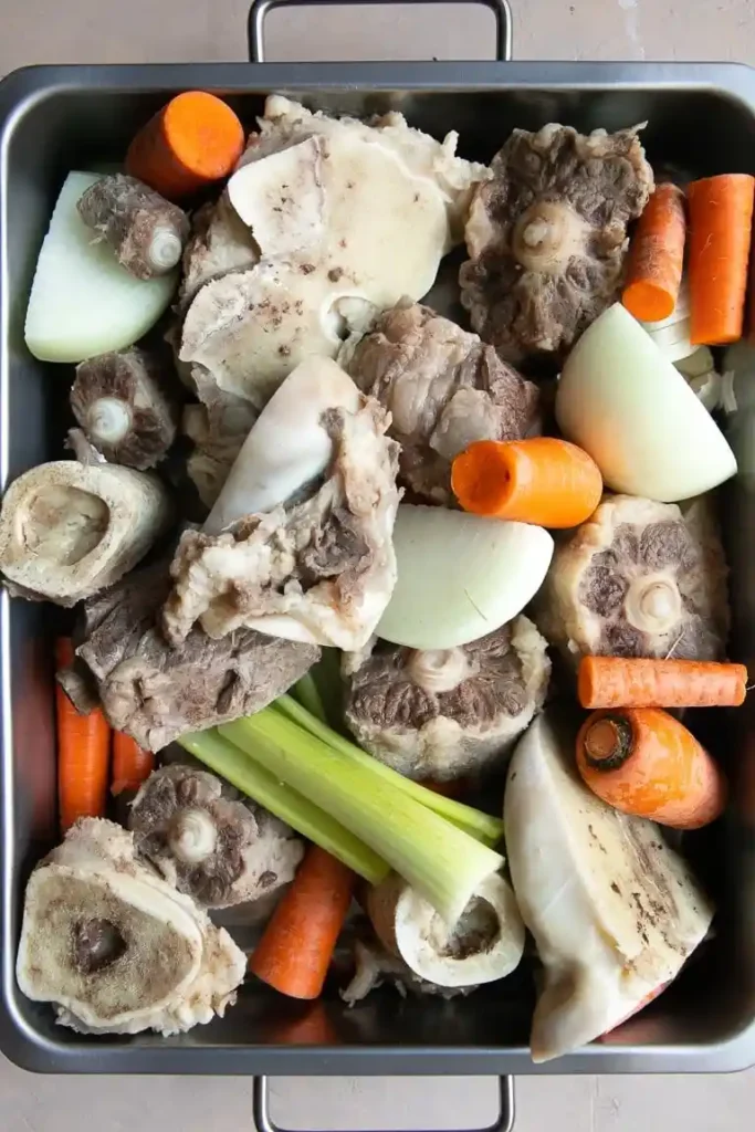 Blanchierte Rinderknochen mit Gemüse in einer Bratform – Vorbereitung für hausgemachte Knochensuppe