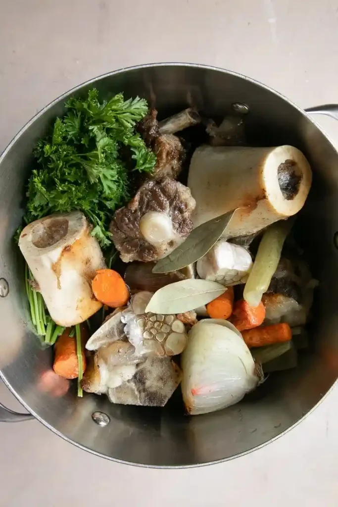 Rinderknochen, Markknochen, Gemüse und Gewürze im Topf als Vorbereitung für hausgemachte Knochensuppe