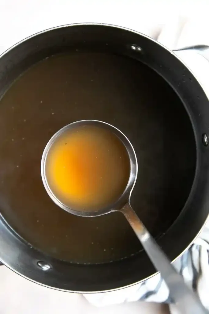 Goldene Rinder-Knochensuppe in einem Topf mit einer Suppenkelle