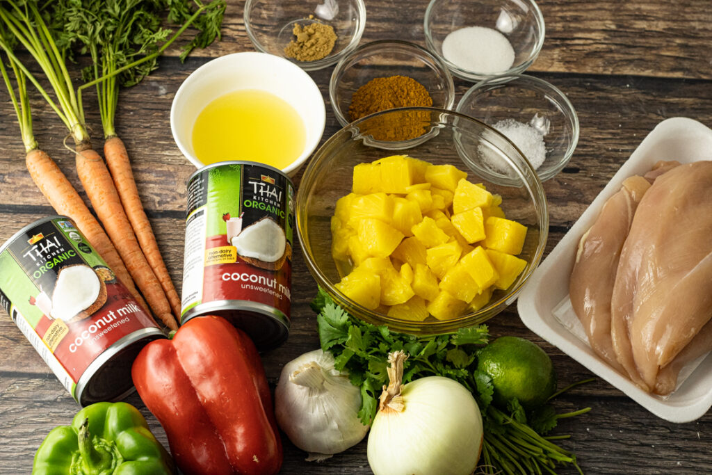 Zutaten für Hähnchen Curry mit Ananas und Kokosmilch auf Holztisch