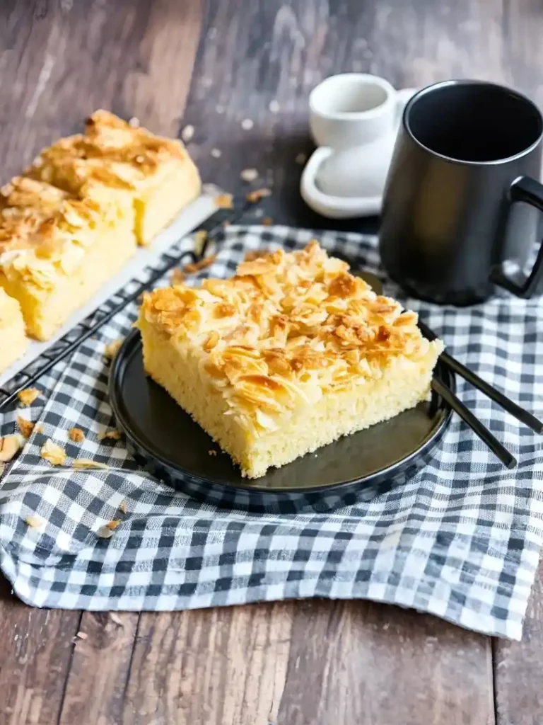 Saftiger Butterkuchen ohne Hefe mit Mandelblättchen auf schwarzem Teller