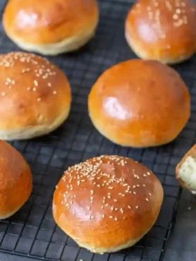 Frisch gebackene Brioche Brötchen und Burger Buns mit glänzender Kruste und Sesam auf einem Gitter zum Abkühlen.